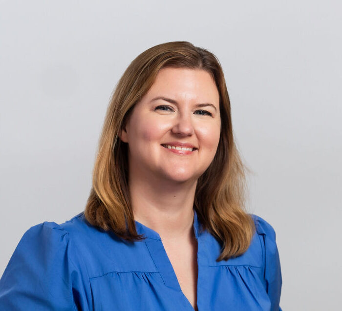 woman with light brown hair wearing a royal blue blouse smiling in a professional headshot
