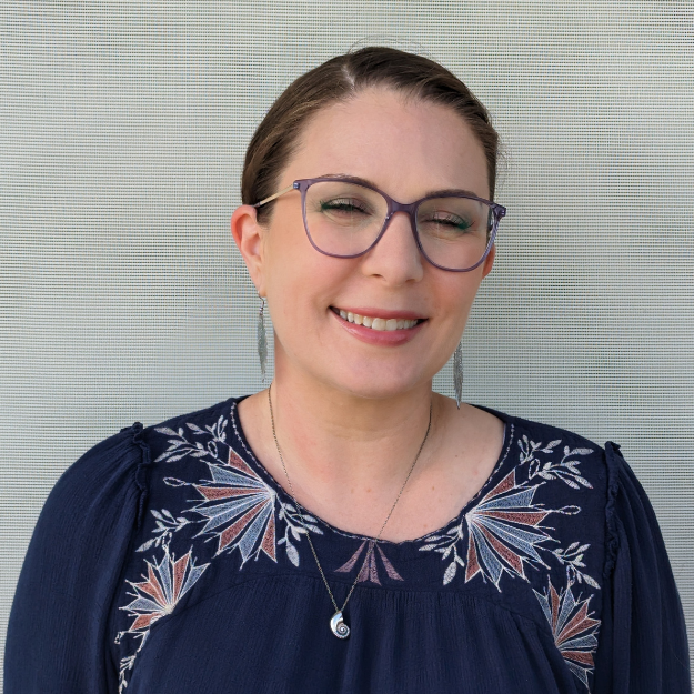 female mental health therapist with purple glasses, a silver necklace, and navy blue patterned shirt smiles in a professional headshot