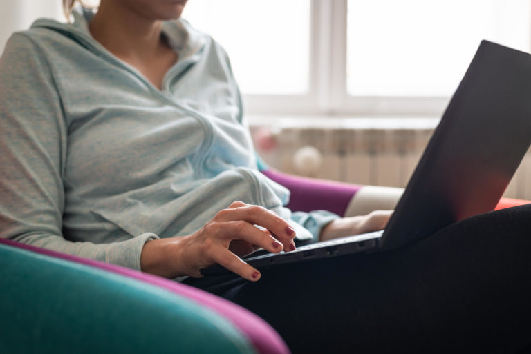A close up of a woman typing on her laptop while sitting in a comfy seat. This could represent the comfort of online therapy for moms in Pennsylvania. Contact us to learn more about postpartum anxiety treatment in Pennsylvania and other services including online therapy in Pennsylvania and more! 17033