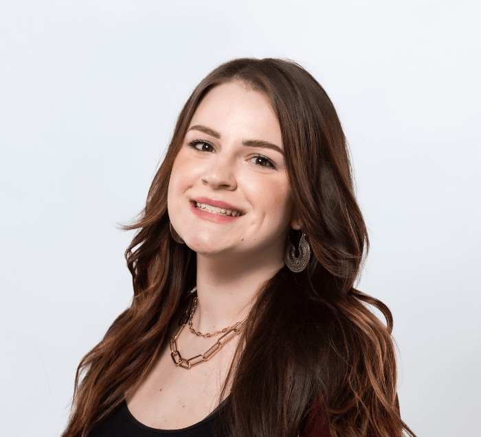 woman with long brown dark hair wearing a scoop neck black blouse, paperclip necklace and round earrings smiles in a professional headshot