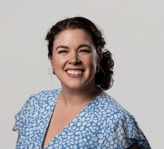 woman with dark hair tied up in back wearig a light blue and white patterned v-neck shirt smiles in a professional headshot