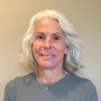 mental health therapist female with white shoulder length hair wearing a light grey shirt and necklace smiles in a professional headshot