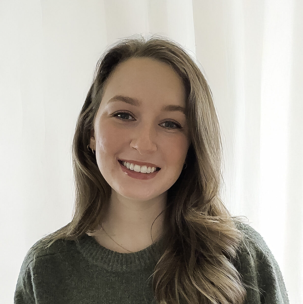 female mental health therapist with long light brown hair wearing a forest green shirt smiles in a professional headshot